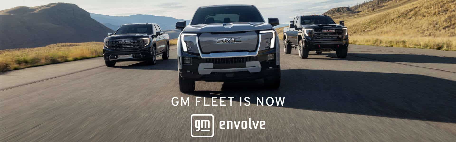 Image of three GMC trucks driving on an open road with scenic mountains in the background, highlighting the GM Fleet and Envolve branding.